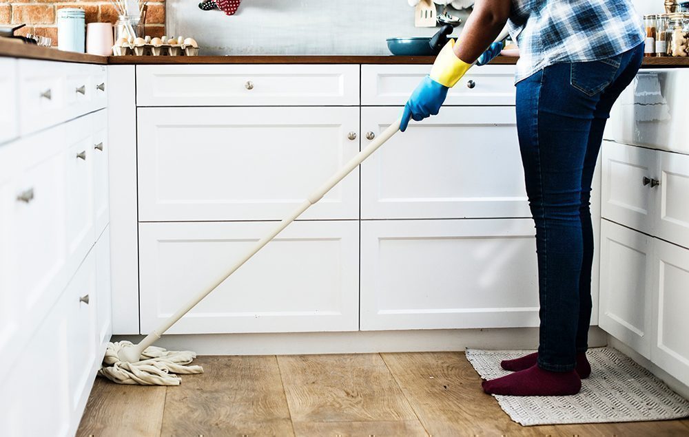 Lady mopping the kitchen floor in front of white units