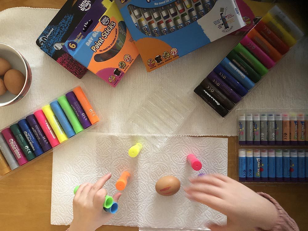 Top view of 2 hands holding paint sticks, ready to paint a hard boiled egg