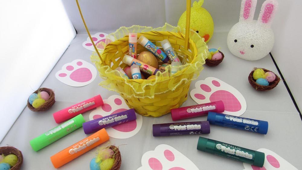 yellow basket of paint sticks and eggs surrounded by more paint sticks, easter nests and bunny footprints