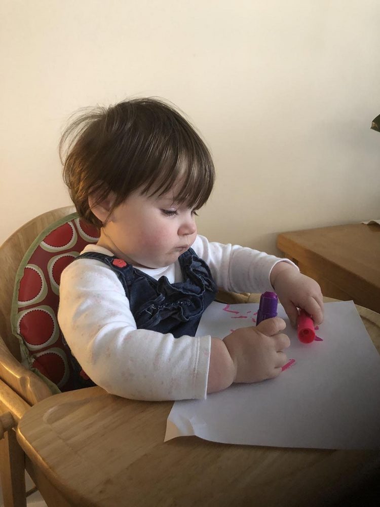 Lottie holding pink and purple paint sticks and a white sheet of paper