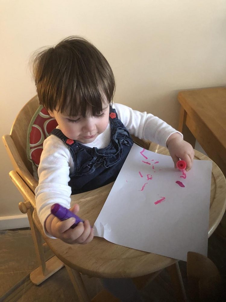 Lottie using paint sticks to paint pink and purple splurges on paper